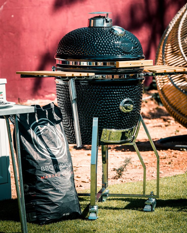 a big green egg sitting on top of a grass covered field next to a bag