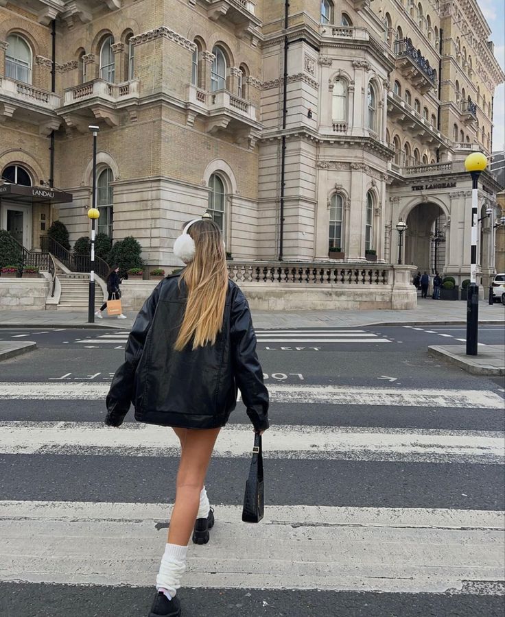 a woman walking across a cross walk in front of a large building