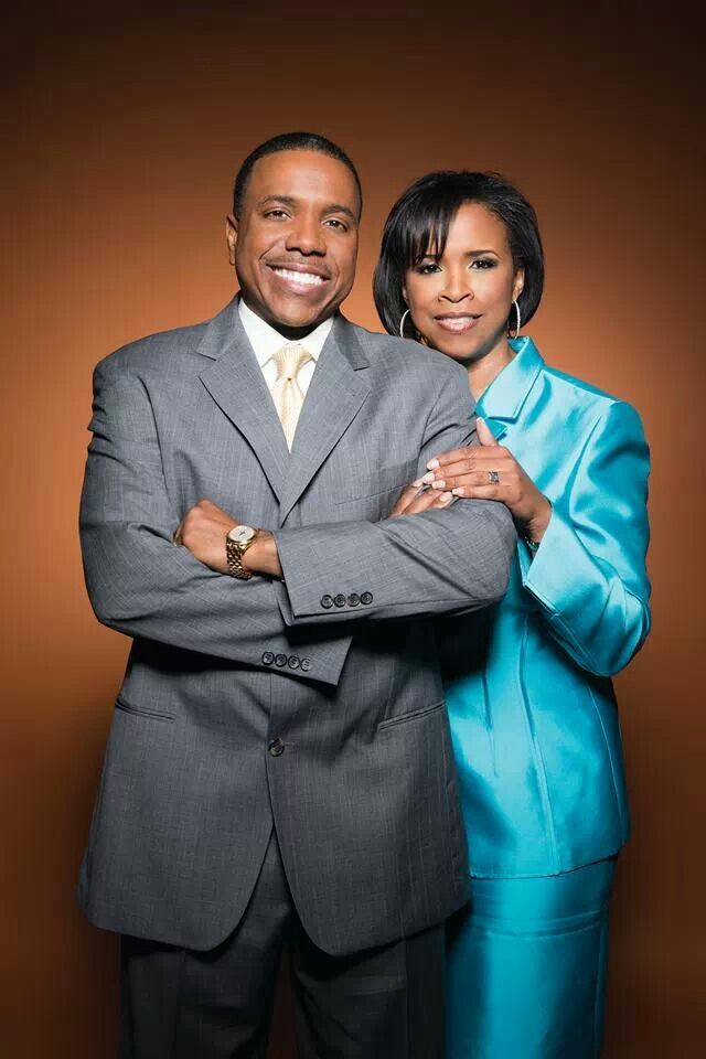 two people standing next to each other in front of a brown background with their arms crossed