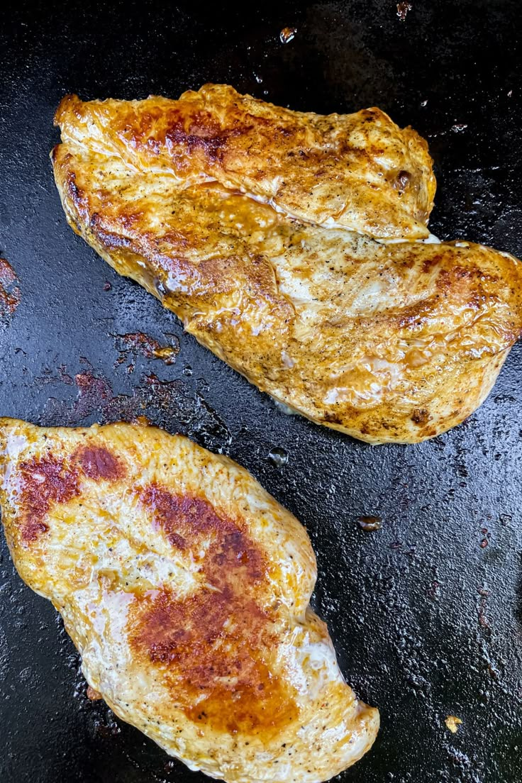 two pieces of meat cooking in a frying pan