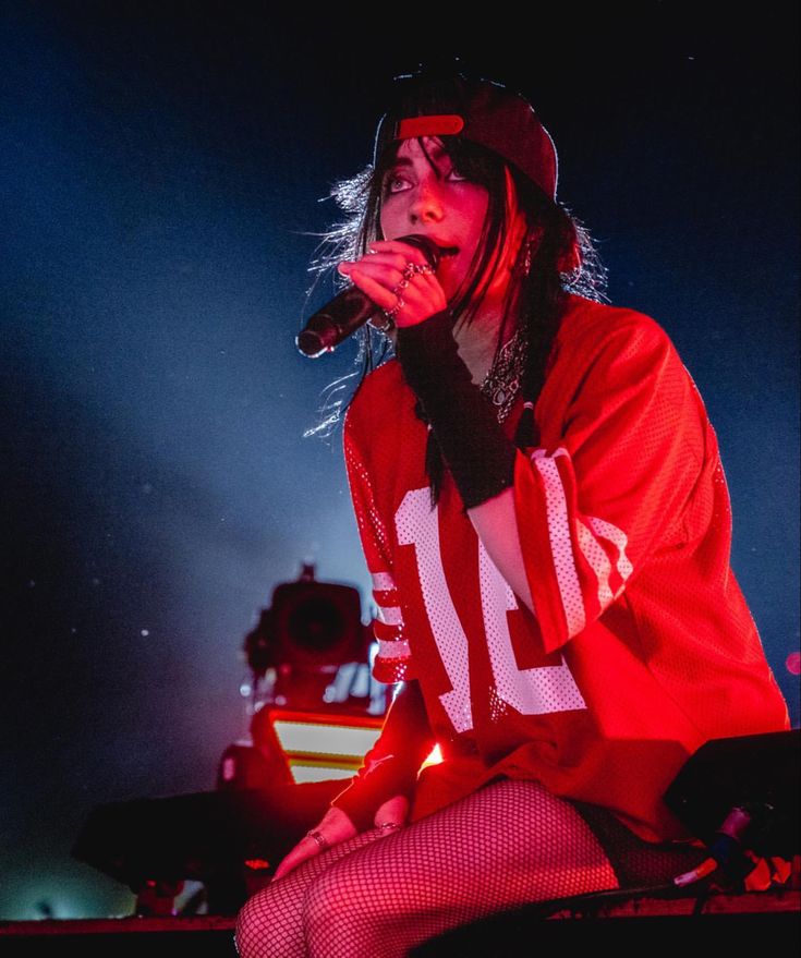 a woman sitting on top of a stool while holding a microphone in her hand and wearing a hat