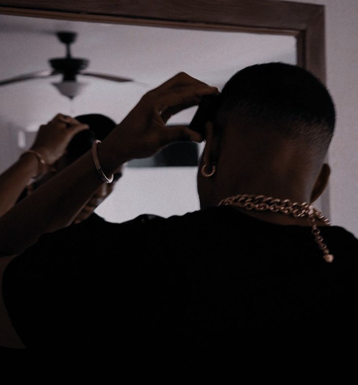 a man is fixing his hair in front of a mirror with a chain around his neck