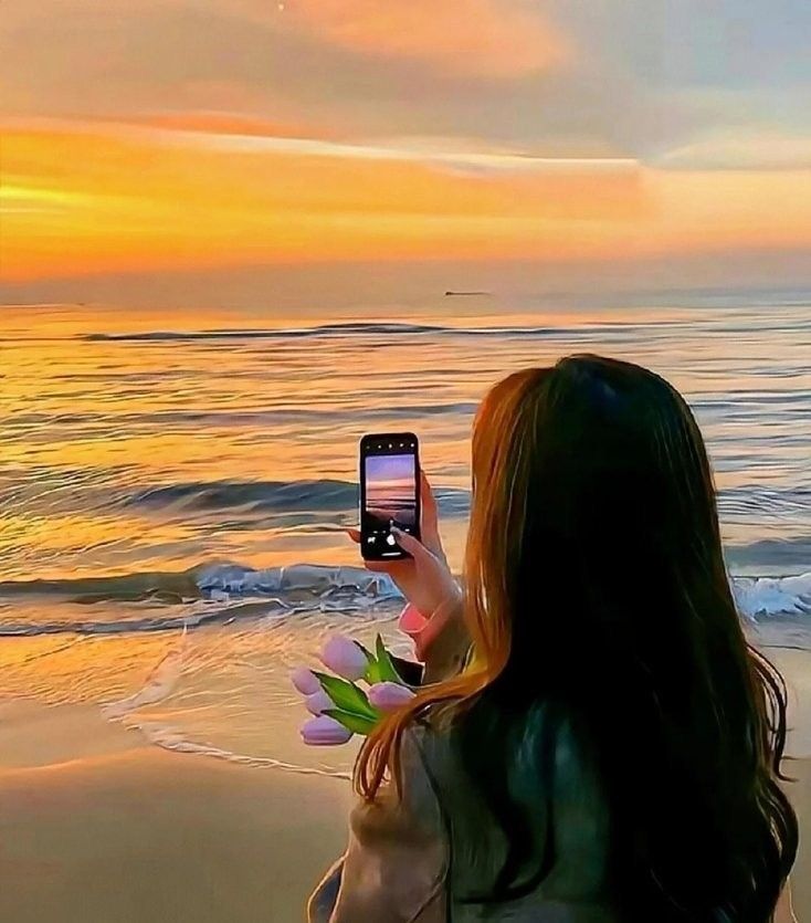 a woman taking a photo with her cell phone on the beach at sunset or sunrise