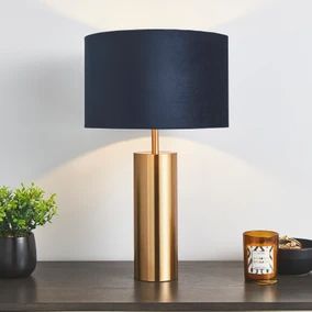 a gold lamp with a black shade on top of it next to a potted plant