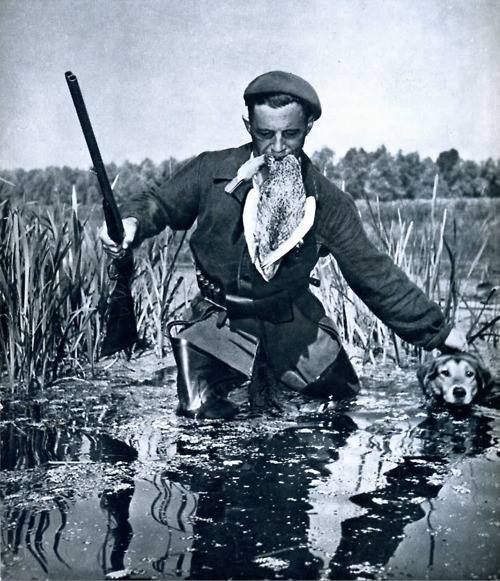 an old black and white photo of a man in the water with his dog holding a fish