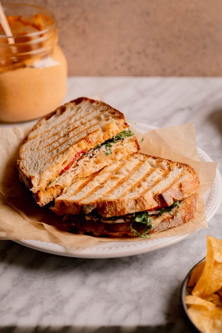 a sandwich cut in half sitting on top of a white plate next to some chips