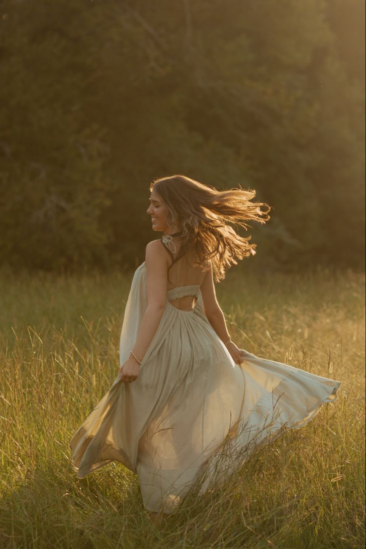 a woman in a dress is walking through tall grass with her hair blowing in the wind