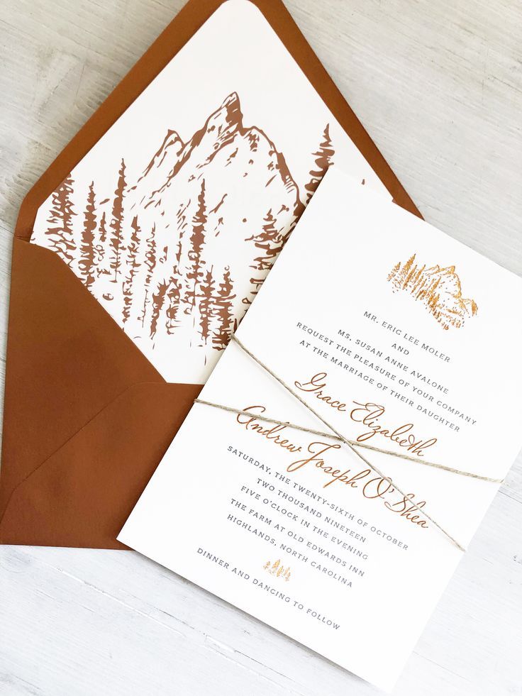 the wedding stationery is set on top of brown envelopes with gold foil lettering