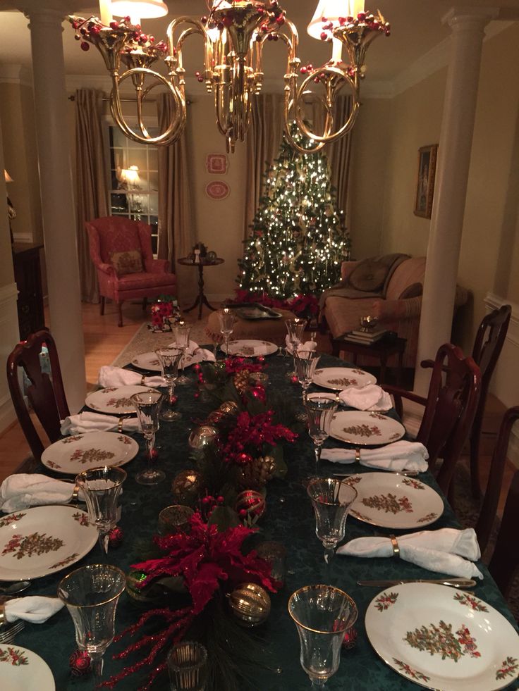 a dining room table set for christmas with plates and silverware on the centerpiece