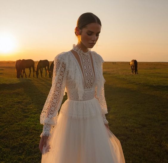 a woman in a white dress standing in front of horses on a field at sunset