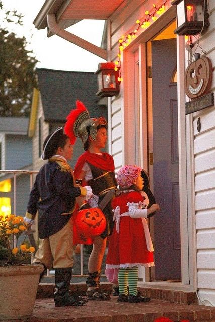 three children dressed up in costumes standing on the front steps of a house with pumpkins