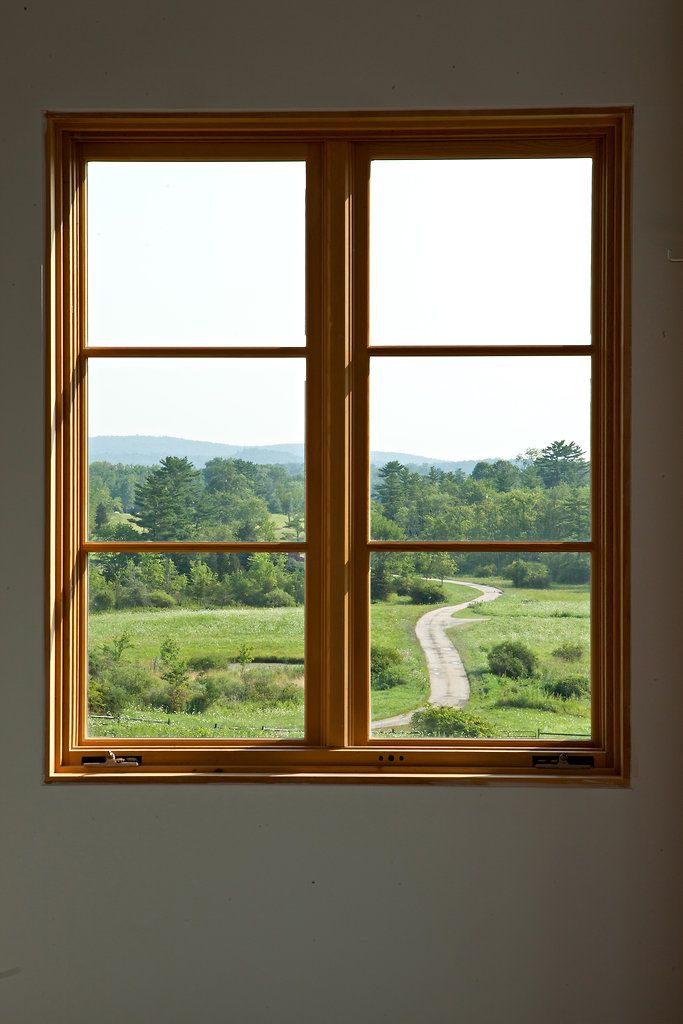 an empty room with two windows looking out on a country road and trees in the distance