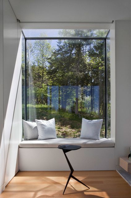 a window seat with two pillows on it in front of a tree filled forest outside