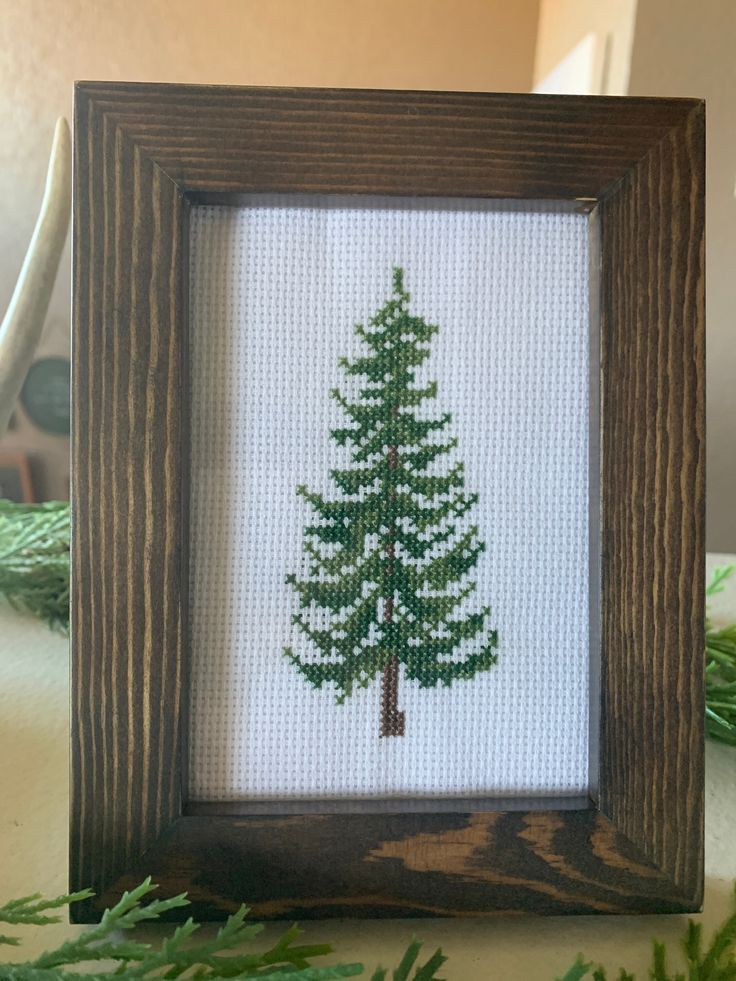 a cross stitch picture frame with a needleed pine tree in the center on a table