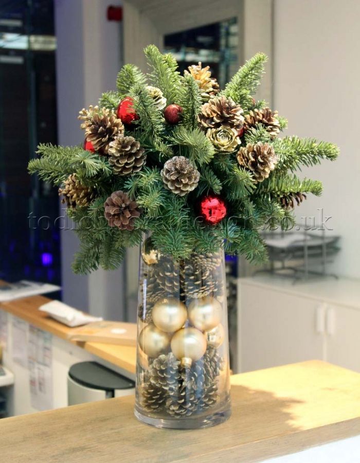 a glass vase filled with pine cones and christmas balls on top of a wooden table