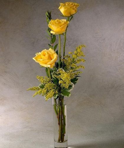 three yellow roses in a clear vase with greenery on the bottom, and other flowers