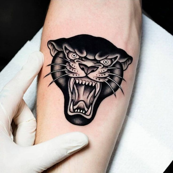 a black and white tattoo of a panther on the left arm with its mouth open