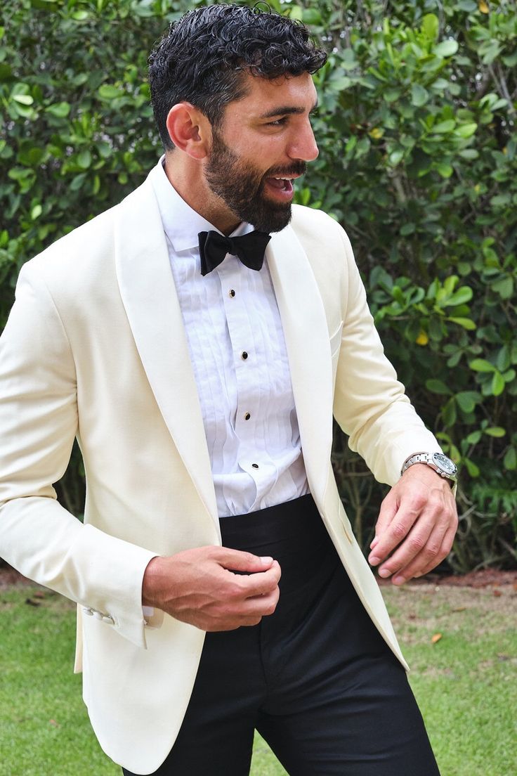 a man in a white tuxedo and black bow tie standing on the grass