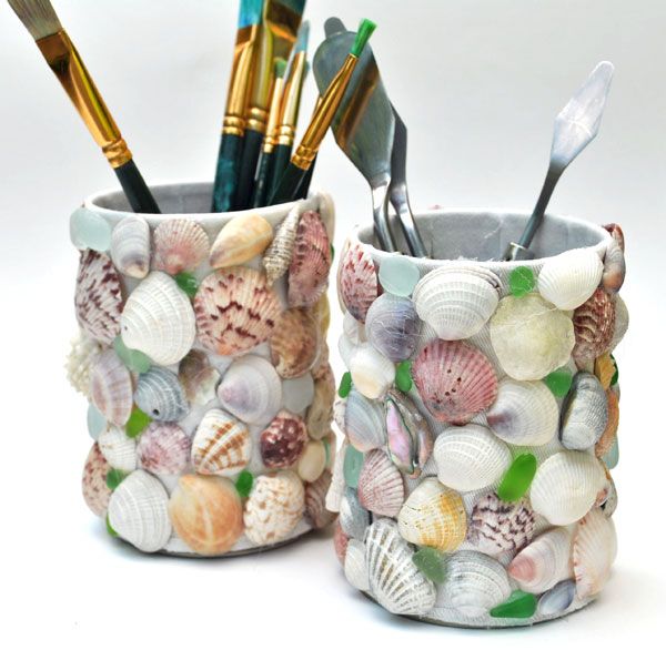 two cups filled with different types of seashells and paintbrushes next to each other