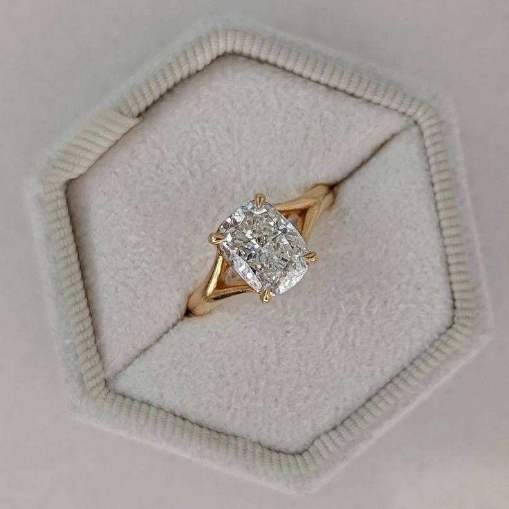 an engagement ring with a cushion cut diamond in a white velvet presentation box on top of a hexagonal surface