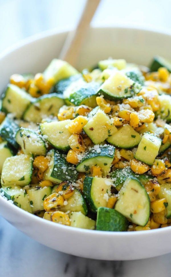 a white bowl filled with cucumber and corn salad on top of a marble counter