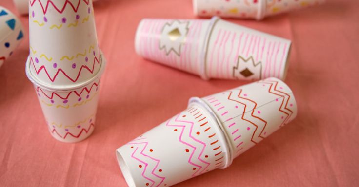 paper cups are lined up on a pink tablecloth with colorful designs and shapes painted on them