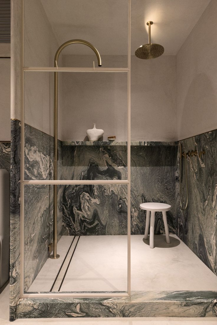 a bathroom with marble walls and flooring, including a walk in shower next to a stool