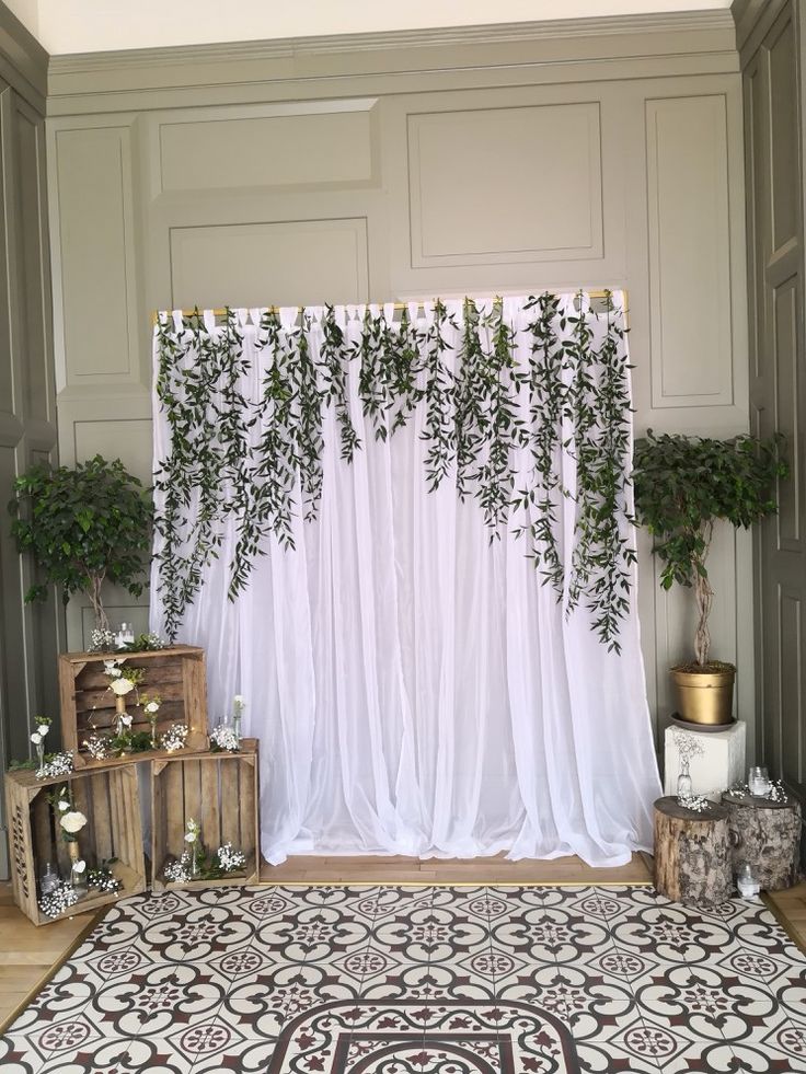 an indoor wedding ceremony with white drapes and greenery hanging over the top of the curtains