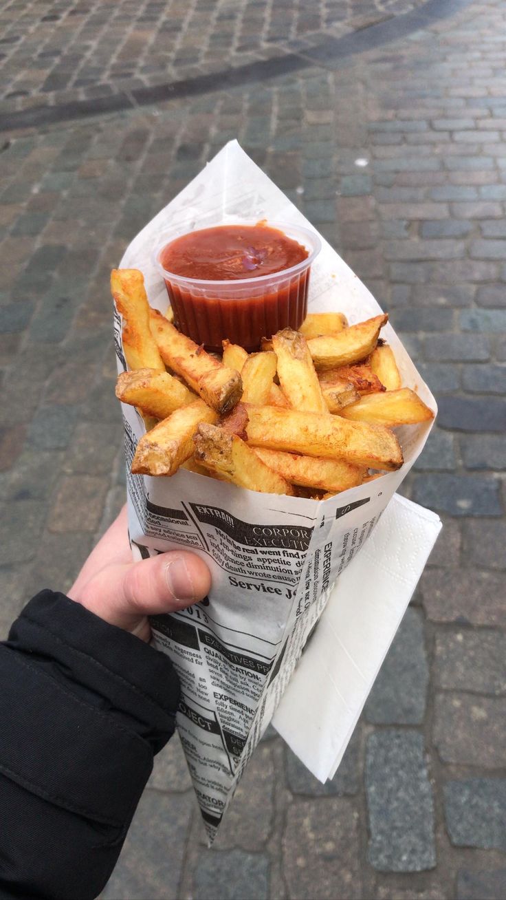 a person holding up a basket full of french fries with ketchup on top