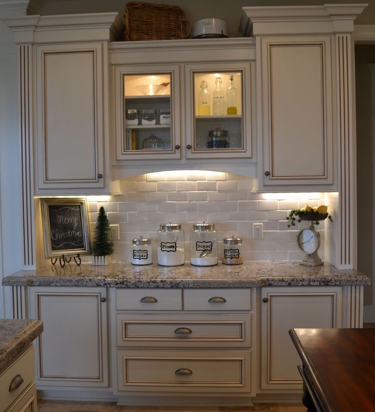 a kitchen with white cabinets and granite counter tops, lights on the cupboards over the stove