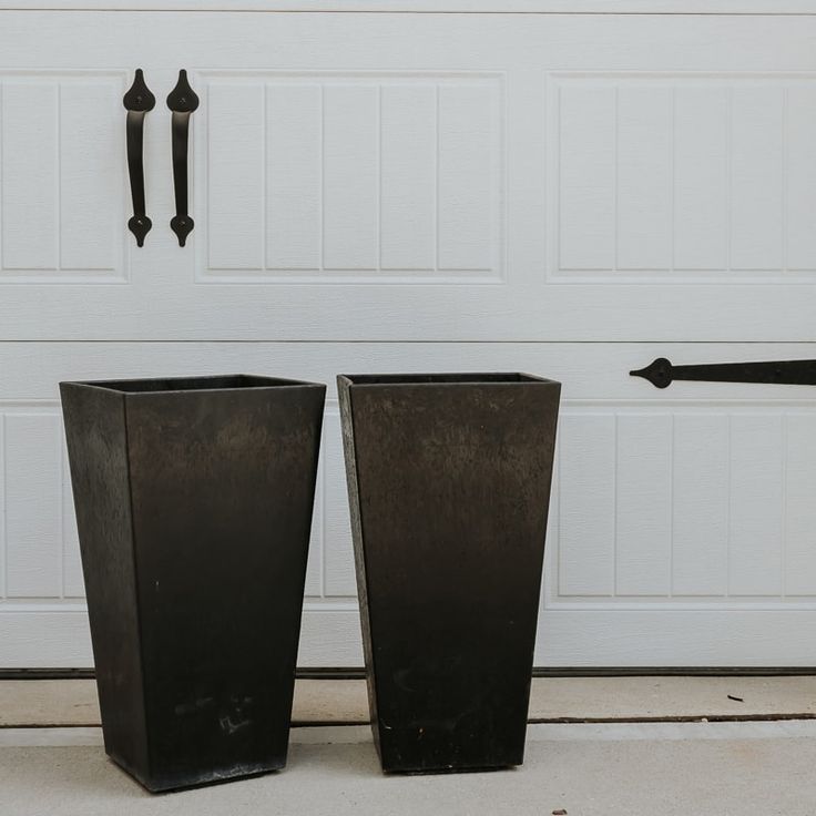 two tall black vases sitting next to each other in front of a garage door