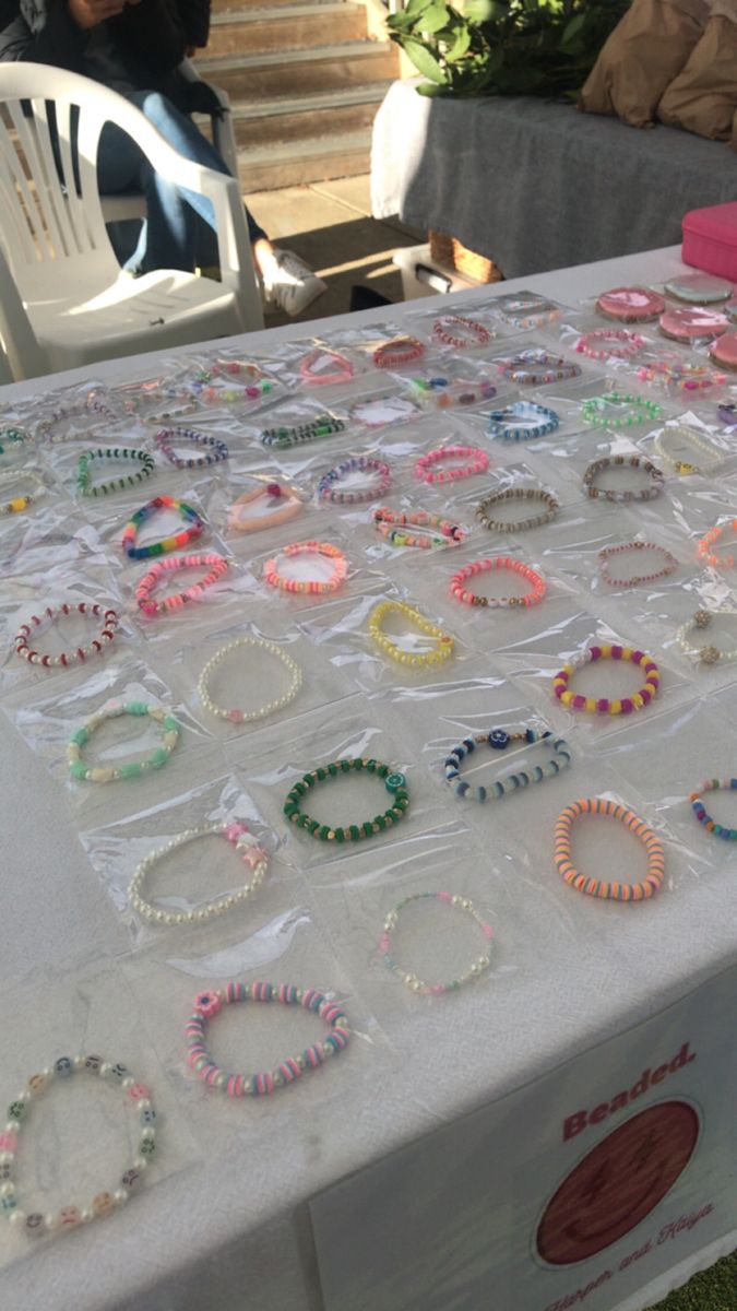 a table covered with lots of bracelets on it's sides and people sitting in the background