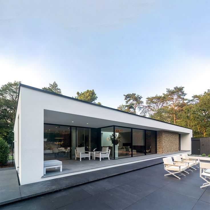 an outdoor patio with chairs and tables on the side of a house that is white