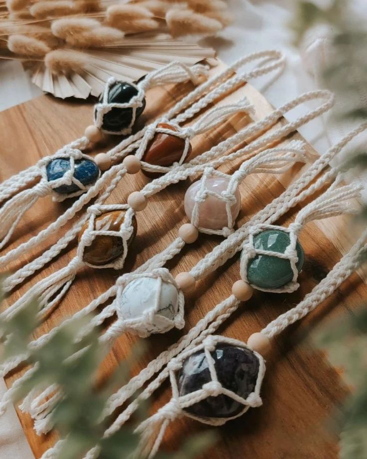 several different colored stones are tied together on a wooden board next to some plants and feathers