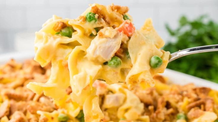 a close up of a spoon full of pasta with peas and chicken on it's side