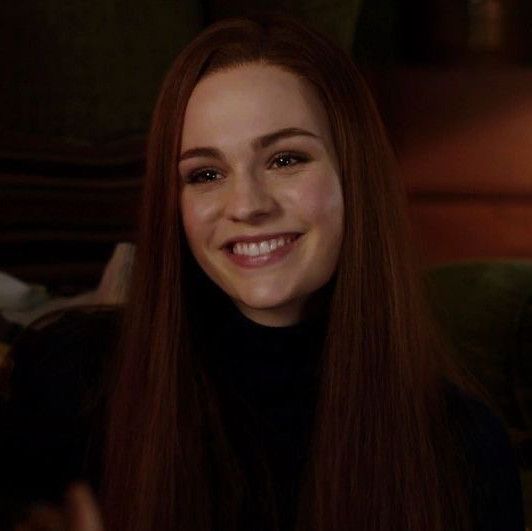 a woman with long brown hair smiling and holding a cell phone in her hand while sitting on a couch