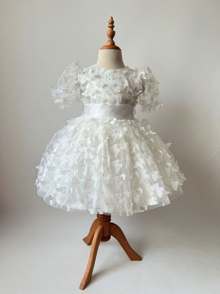 ✿ABOUT THIS DRESS ✓The fluffy skirt and 3D butterflies of our handmade dress make it a standout piece that will delight any little girl.  ✓The dress is lined with cotton to ensure your child's comfort.  ✓With its girly charm and attention to detail, this dress is sure to become a favorite for any child who loves to dress up and feel special. ✿FABRIC INFORMATION ✓Natural cotton lining 100% under the skirt, satin, tutu, and tulle with a 3D butterfly on the top. ✓Color of your item may vary slightl Cute Short Sleeve Baptism Dress For Party, White Tutu Dress With Bow For Birthday, White Tutu Dress With Ruffles And Short Sleeves, White Short Sleeve Tutu Dress With Ruffles, White Ruffled Short Sleeve Tutu Dress, Cute Floral Applique Tutu Dress For Party, White Tutu Dress With Floral Applique For Baptism, White Princess Dress With Floral Applique, Short Sleeve Tutu Dress With Ruffles For Baptism