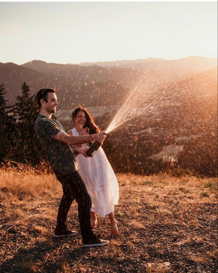 a man and woman are standing in the grass spraying water on each other with their hands