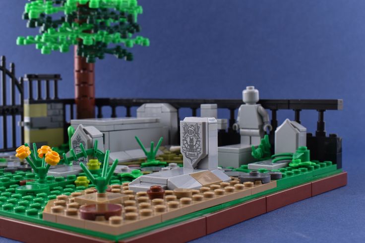 a lego model of a cemetery with flowers in the foreground and a tree on the other side