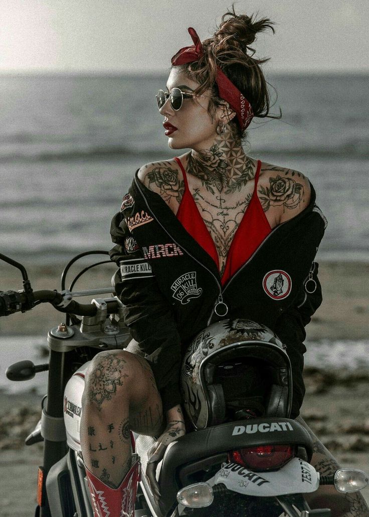 a woman sitting on top of a motorcycle next to the ocean with her tattoos and piercings