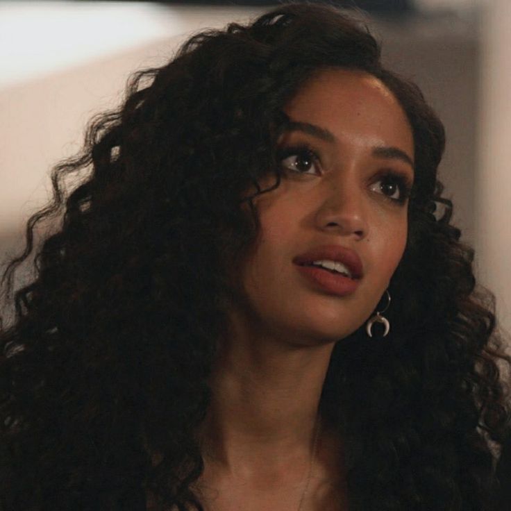 a close up of a person with long curly hair and wearing earrings looking off to the side