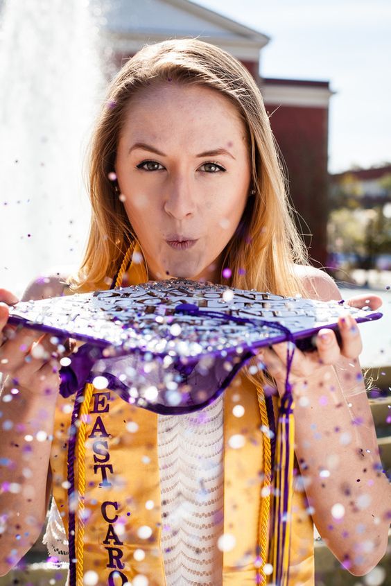 a woman in yellow jacket blowing confetti on top of her face with purple ribbon