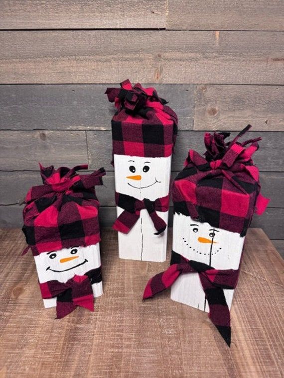 three snowmen wrapped in red and black plaid paper on top of a wooden table