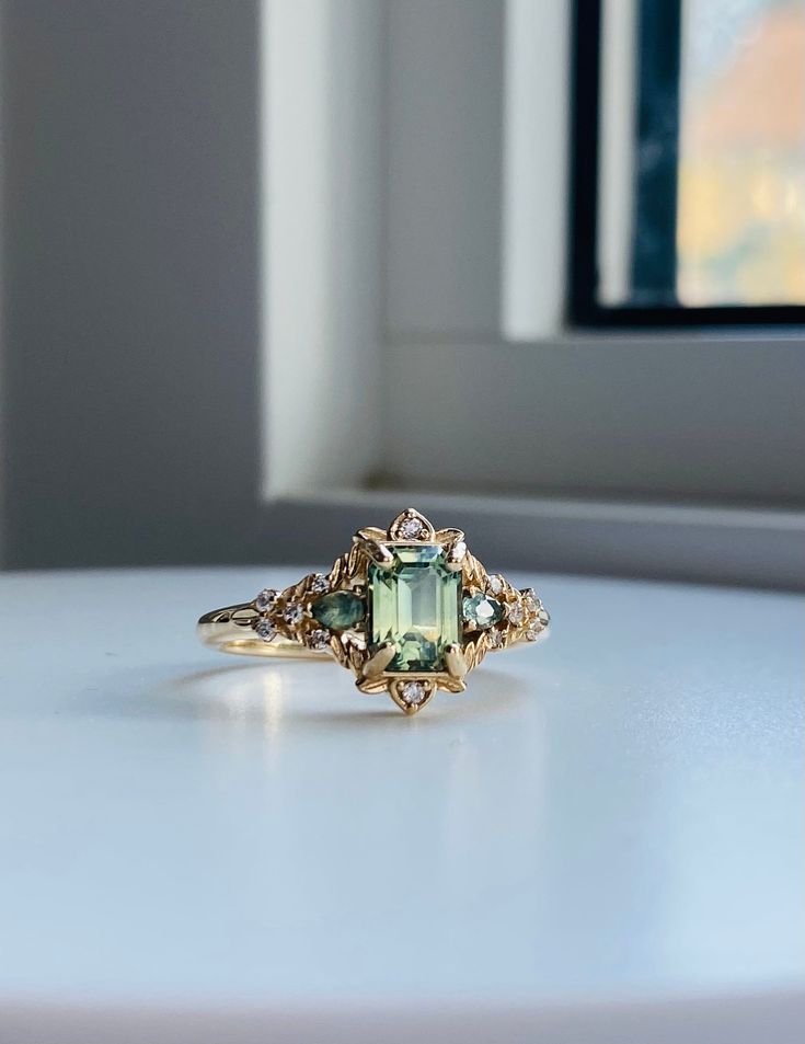 an engagement ring with a green tourmaline surrounded by small diamonds on a white surface