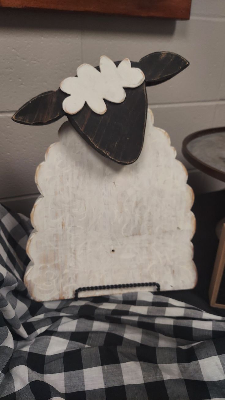 a wooden sheep with white flowers on it's head sitting on a black and white checkered blanket