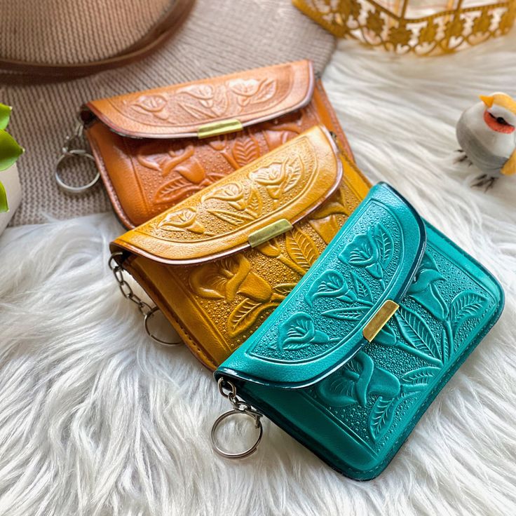 three different colored purses sitting on top of a white fur covered floor next to a bird