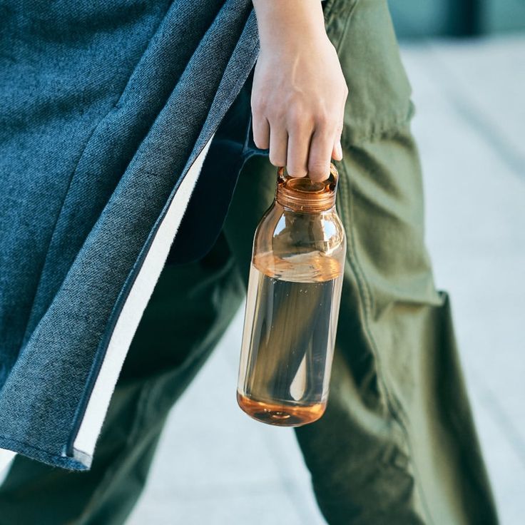 a person carrying a bottle with something in it on the street and wearing green pants