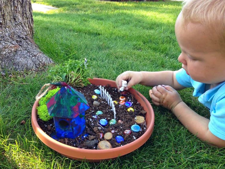 a toddler playing with a potted plant in the grass