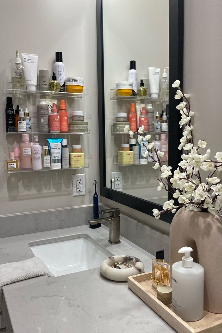 a bathroom sink with bottles and soaps on the shelves above it, along with a vase filled with flowers