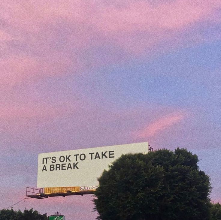 a billboard that says it's ok to take a break in front of some trees